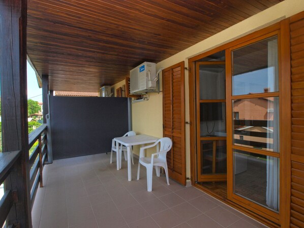 A covered outdoor patio with a wooden ceiling, a table and chairs, and a sliding glass door leading to an interior space.