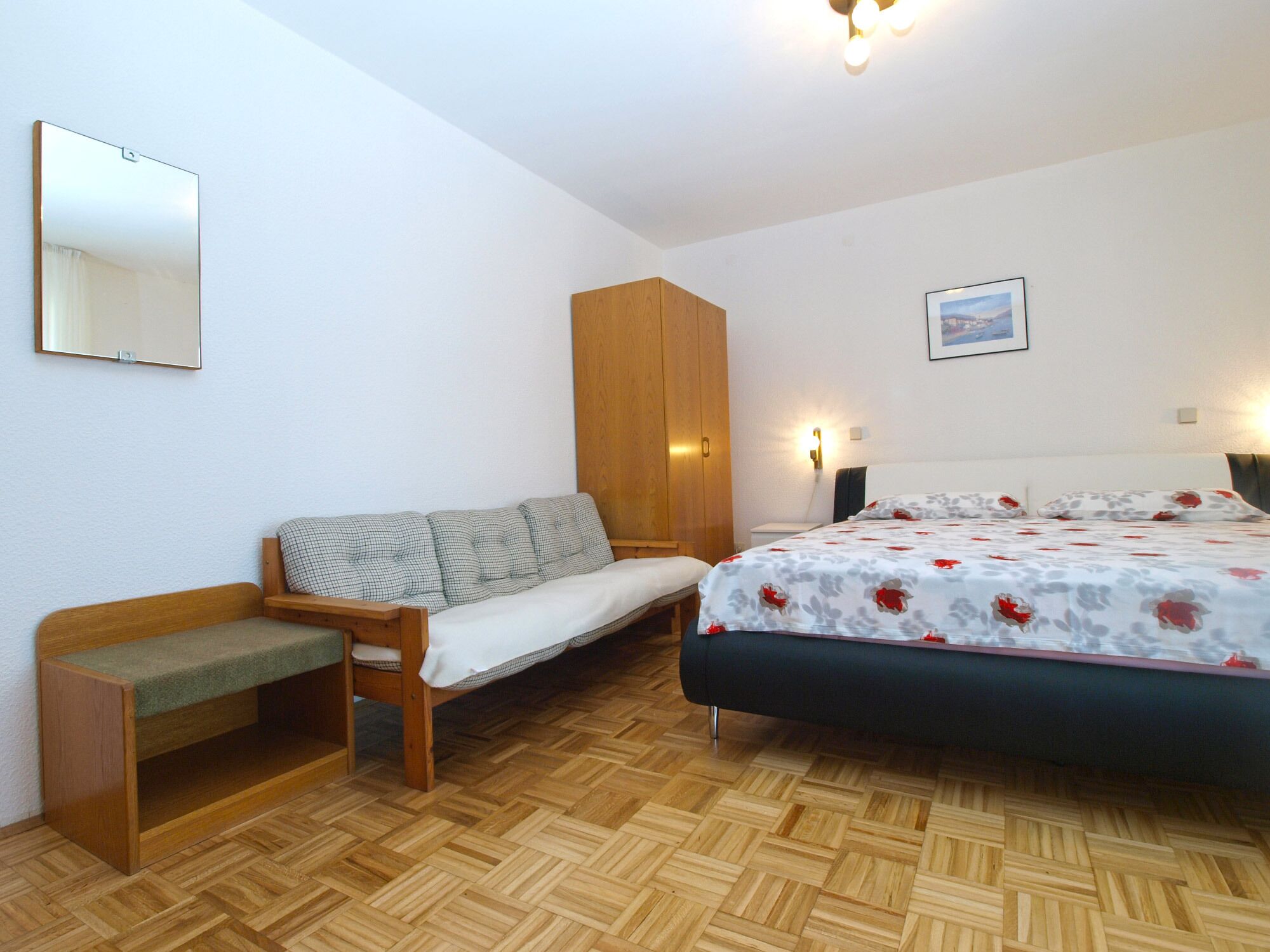 Un dormitorio con cama, sofá, armario de madera, banca, espejo y lámpara de pared.