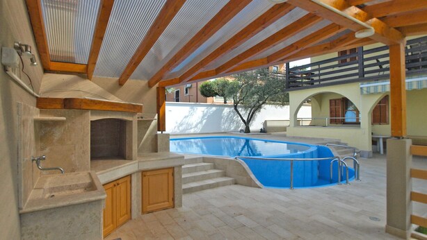 An outdoor pool area with a stone fireplace, wooden deck, and a covered seating area. - Apartment 1624/16706 (Istria - Novigrad), 600m from the beach (Novigrad)