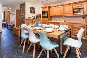 A modern kitchen with wooden cabinets, a dining table set for six, and a stone accent wall.