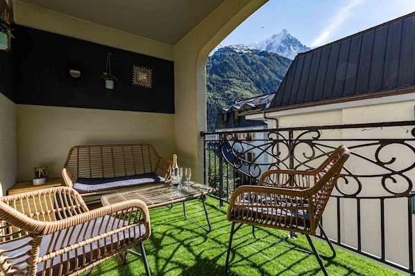 Un balcon agrémenté de meubles en osier, une table avec des verres et une vue sur les montagnes.