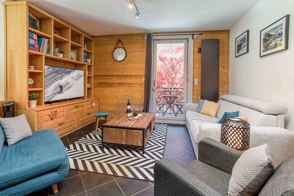 A living room with a television, wooden shelves, a sofa, a coffee table, and a patterned rug.