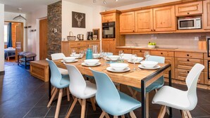 A modern kitchen with wooden cabinets, a dining table set for six, and a stone accent wall. - Le Paradis 25 Apartment -  an apartment that sleeps 6 guests in 3 bedrooms (Chamonix-Mont-Blanc)
