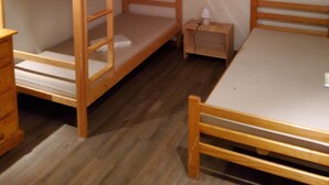 Ein Zimmer mit zwei Etagenbetten, einem kleinen Tisch, einem Nachttisch und einem Fenster mit Vorhängen.