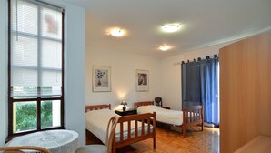 Una camera da letto con due letti di legno, un tavolino, una sedia e una finestra con persiane.
