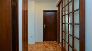Un corridoio con una porta in legno, una finestra con telaio in legno e vetro smerigliato, e un pavimento a spina di pesce.