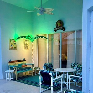Une pièce avec un ventilateur de plafond, une enseigne indiquant « Margaritaville », une petite table avec des chaises, un banc et une plante décorative.