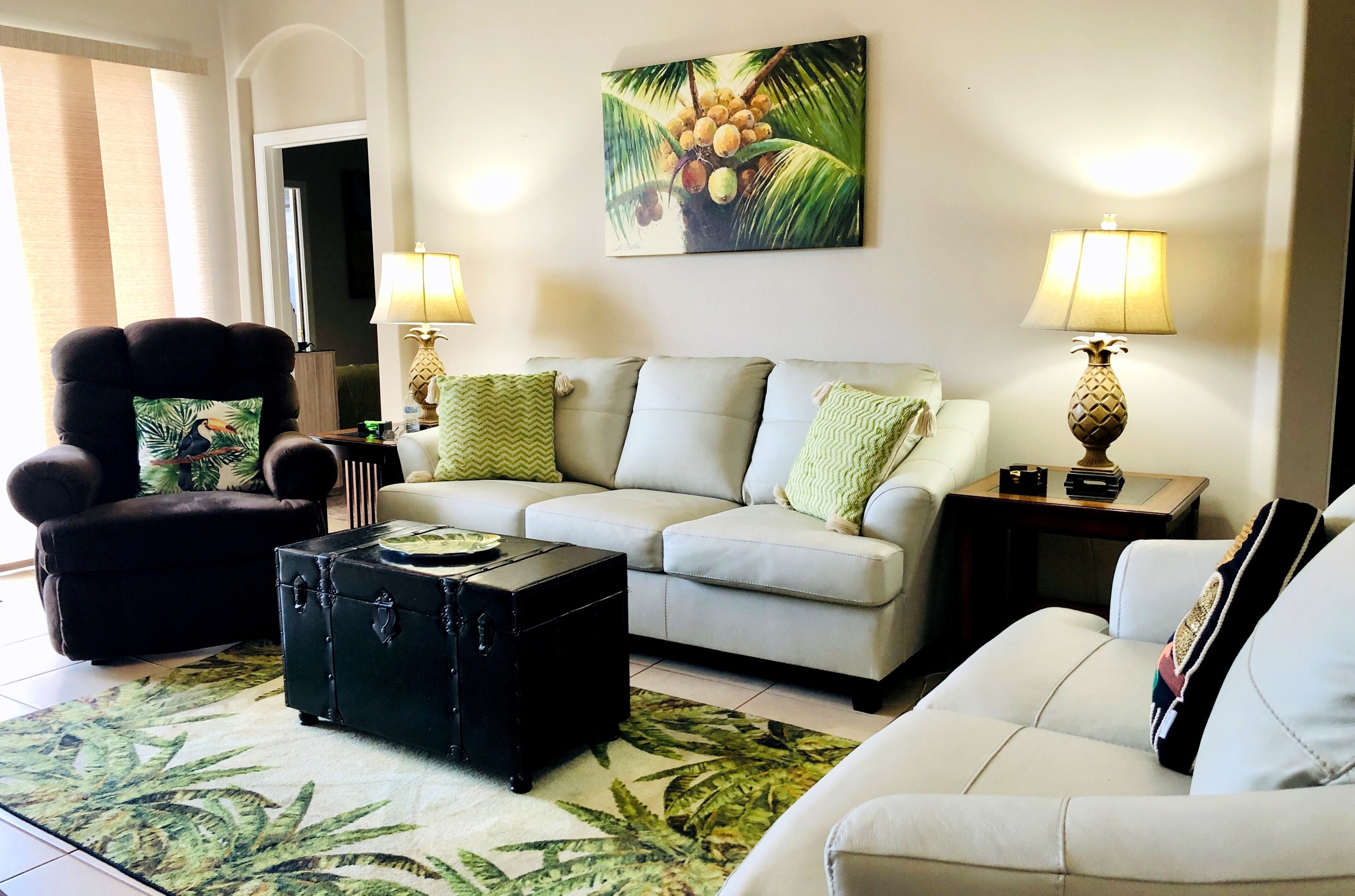 A living room with a sofa, armchair, and a coffee table. There is a painting on the wall and two lamps on side tables.
