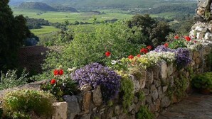 Een stenen muur met een tuin in een landelijke omgeving, met uitzicht op een vallei met velden en heuvels.