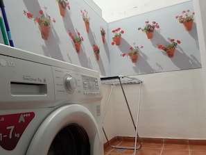Un área de lavandería con una lavadora blanca, un tendedero y una pared decorada con plantas en macetas.