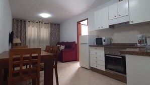 Une cuisine compacte avec des meubles blancs, un four à micro-ondes, une machine à café et un coin repas comprenant une table et des chaises.