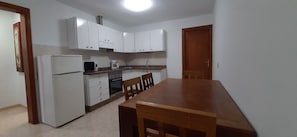 Una cocina compacta con alacenas blancas, un refrigerador, un microondas, un horno y una mesa de comedor con sillas.