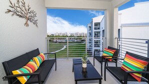 A balcony with black furniture, colorful striped cushions, and a decorative metal piece on the wall.