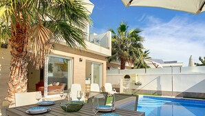 Ein Essbereich am Pool mit einem Tisch für vier Personen, umgeben von Palmen und einem klaren, blauen Pool.