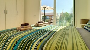Ein Schlafzimmer mit einem großen Bett, einem Sessel, einer Couch und Blick ins Freie.