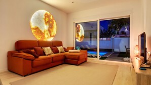Ein modernes Wohnzimmer mit einer Eckcouch, einer großen, runden Wanddekoration und einer Glasschiebetür, die zu einem Poolbereich führt.