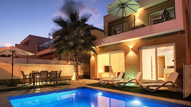 Ein Swimmingpool mit Liegestühlen und einem Tisch, umgeben von einem Gebäude mit Balkon und einer Palme.