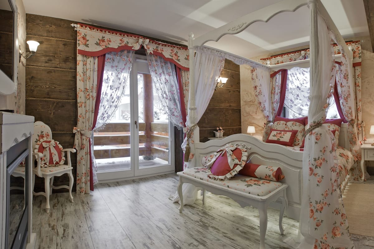 Un lit à baldaquin à quatre poteaux, agrémenté d’une literie à motifs floraux, doté d’un plancher en bois et offrant une vue sur l’extérieur grâce à une porte coulissante.