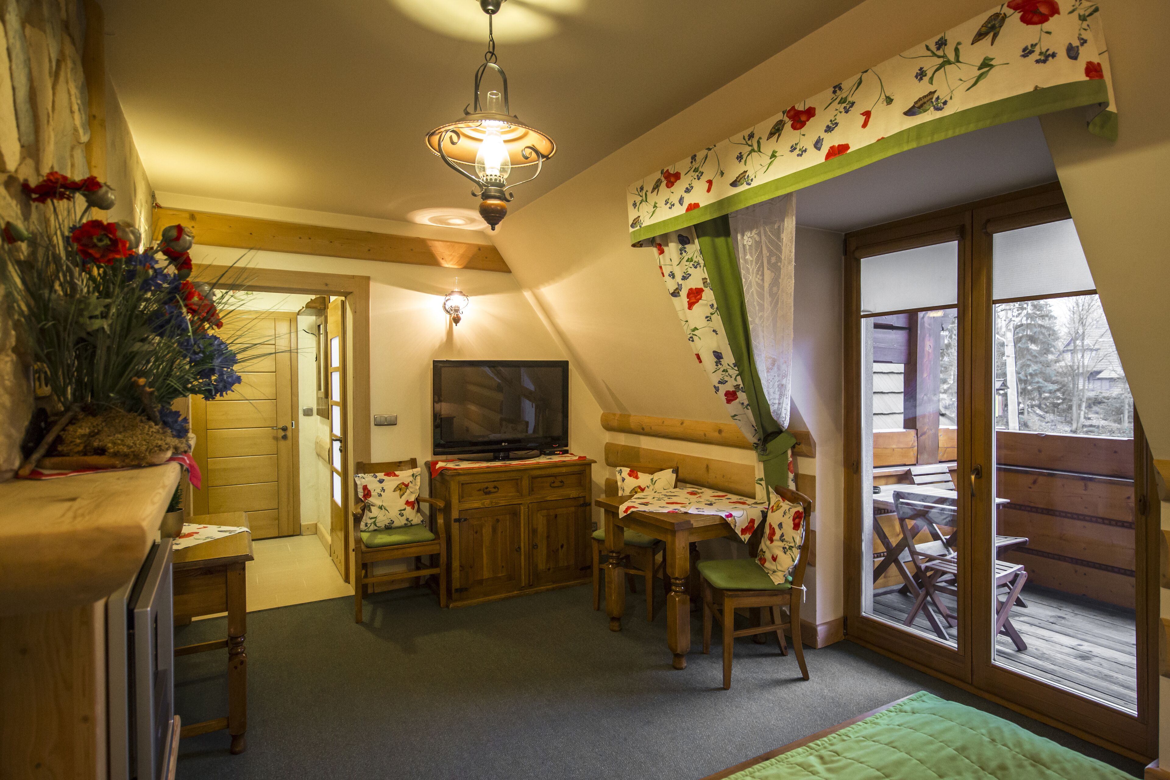 A cozy room with a television, wooden furniture, a green rug, and a view of the outdoors through a glass door.
