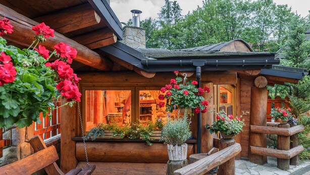 A rustic log cabin with a wooden porch, stone steps, and hanging flower baskets. - Lesny Dworek (Zakopane)