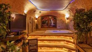 A spa area with a stone wall, a bathtub, and a television. - Lesny Dworek (Zakopane)