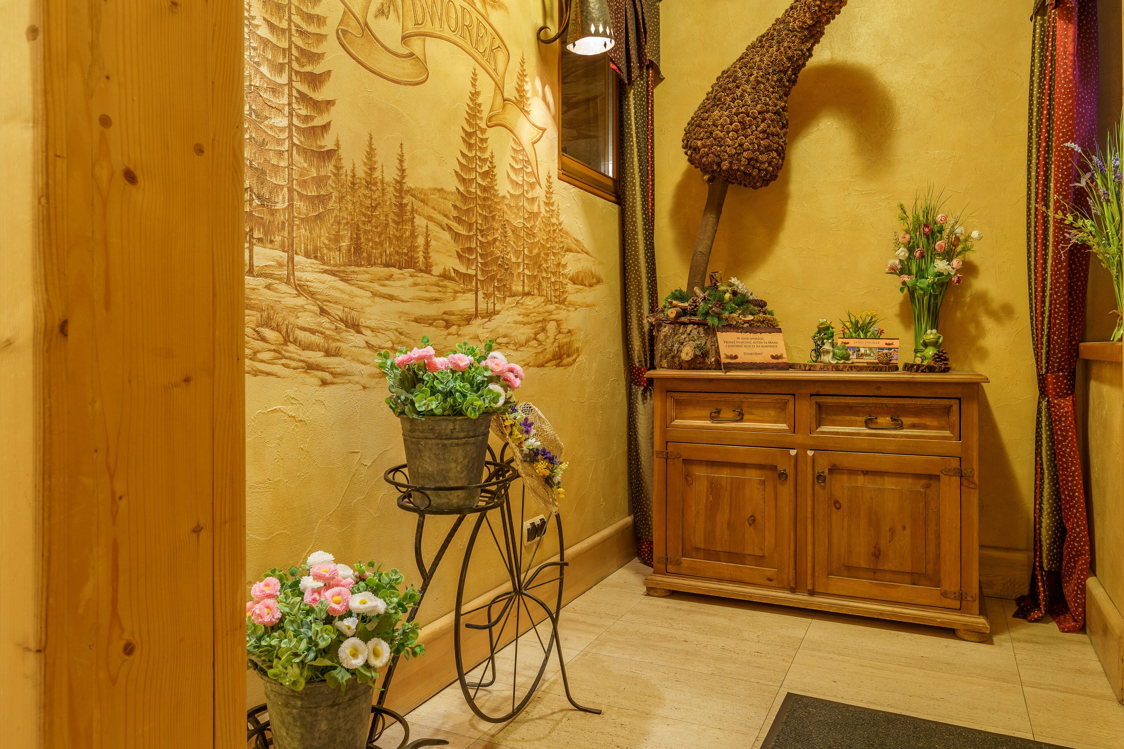 A wooden cabinet with drawers, a wall with a carved tree design, and two potted plants with flowers.