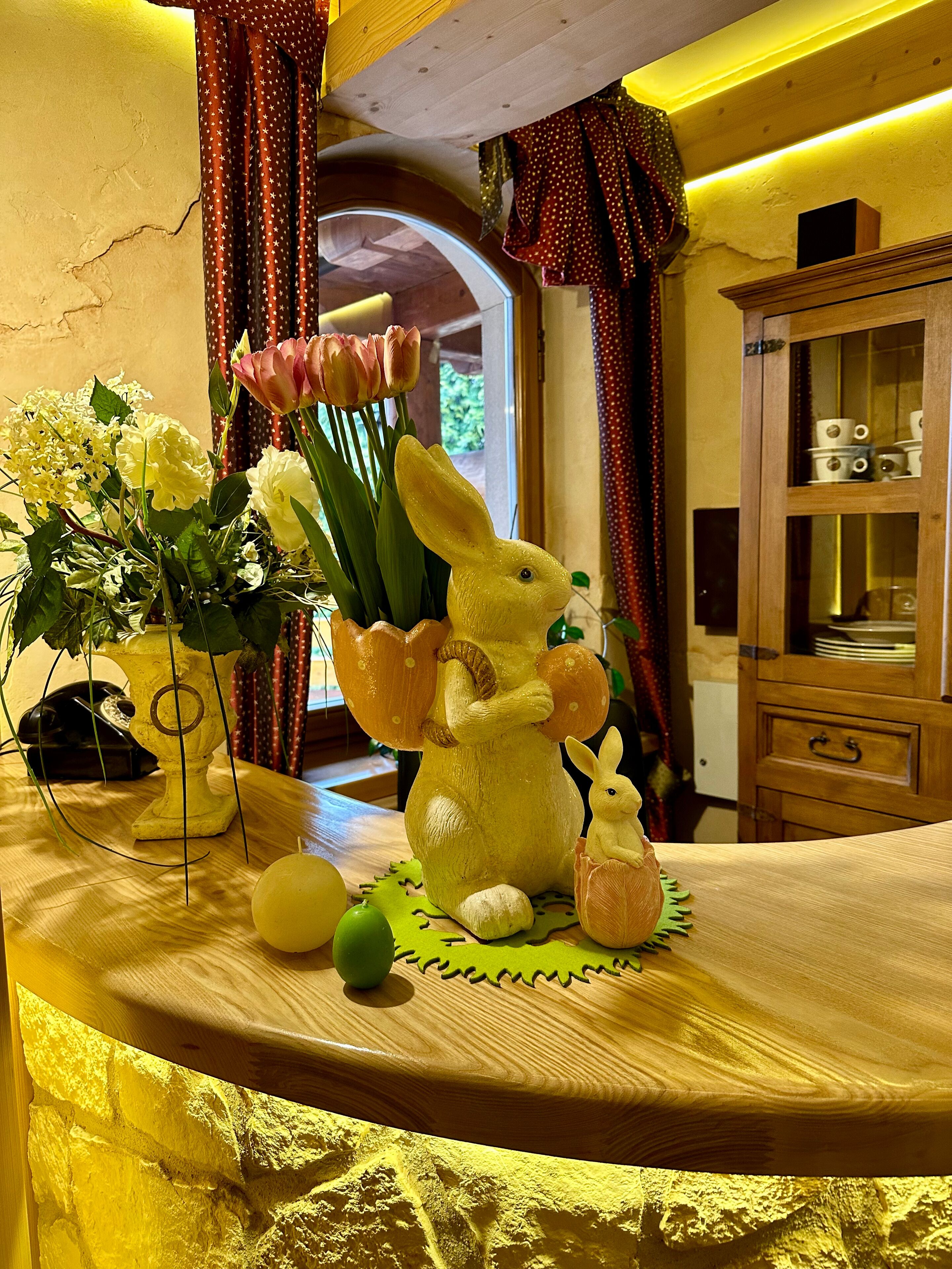 Una mesa con una figurita de conejo de cerámica, un florero de flores y una manzana verde.