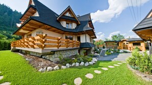 A chalet-style house with a stone foundation, wooden deck, and a stone pathway leading to the entrance. - Lesny Dworek (Zakopane)
