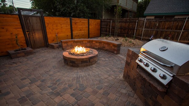Un patio trasero con un hogar, una parrilla y una valla de madera.