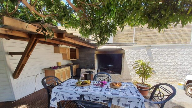 Un área de comedor al aire libre con una mesa bajo una pérgola, una parrilla y una planta en maceta.