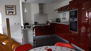 Una cocina compacta con armarios rojos, una estufa a gas, un horno y un comedor con mesa y sillas.