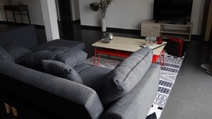 Una sala moderna con un sofá gris, una mesa de centro de madera, una planta pequeña y un televisor sobre un mueble.
