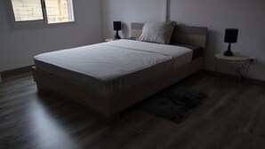 Un dormitorio con una cama, dos lámparas de noche, un ventanal y una pequeña mesa redonda con lámpara.