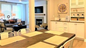 A modern living room with a sofa, coffee table, and TV. A dining area with a table and chairs is adjacent to the living room.