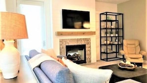 A living room with a sofa, a coffee table, a fireplace, a TV, and a bookshelf.