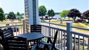 A balcony with outdoor seating and a view of a parking lot and trees.