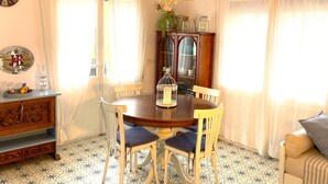 Un coin repas comprenant une table ronde, quatre chaises, un lustre, un buffet et une horloge murale.