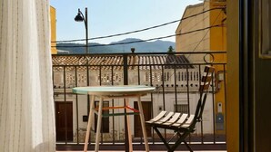 Un balcon avec une table et une chaise, une vue sur un immeuble avec un toit en tuiles, et une montagne en arrière-plan.