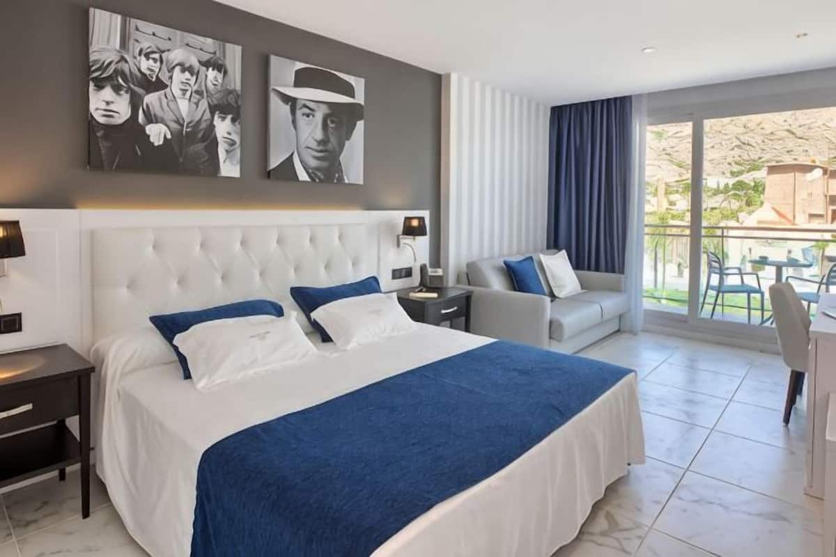 A hotel room with a large bed, a sofa, a dining table, and a balcony with a view.