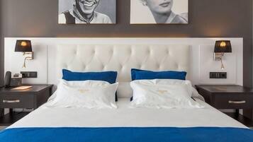 A hotel room with a large bed, two bedside tables, a nightstand, a wall-mounted lamp, and two framed pictures on the wall.