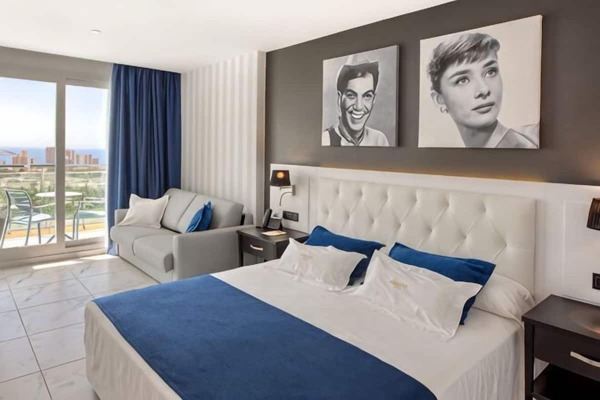 Ett hotellrum med en stor säng, en soffa, ett nattduksbord och utsikt över staden.