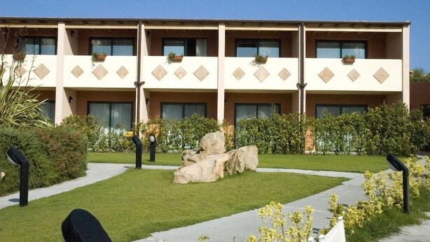 A multi-story hotel with a symmetrical facade, large windows, and a central courtyard with a rock feature and greenery. - Hotel Club Baja Bianca (San Teodoro)