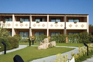 Un hôtel à plusieurs étages, doté d’une façade symétrique, de grandes fenêtres et d’une cour intérieure agrémentée d’un élément rocheux et de verdure.
