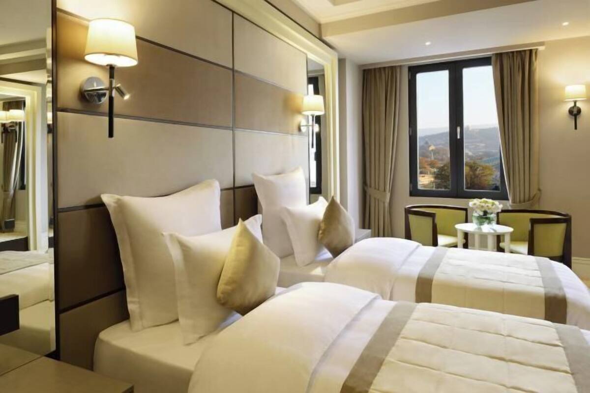 A hotel room with two beds, a view of the city, and a small table with a vase of flowers.