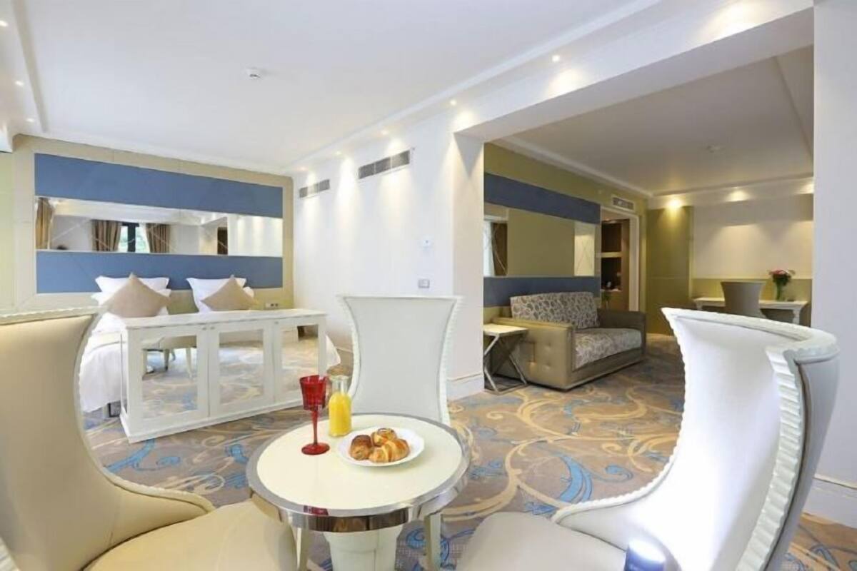A hotel room with a bed, a dining area with a table and chairs, a sofa, and a small kitchen area.