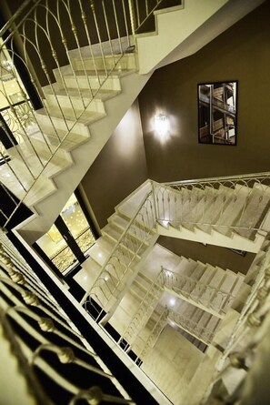 Un intérieur à plusieurs niveaux avec un escalier central, un tableau encadré au mur et un lustre.