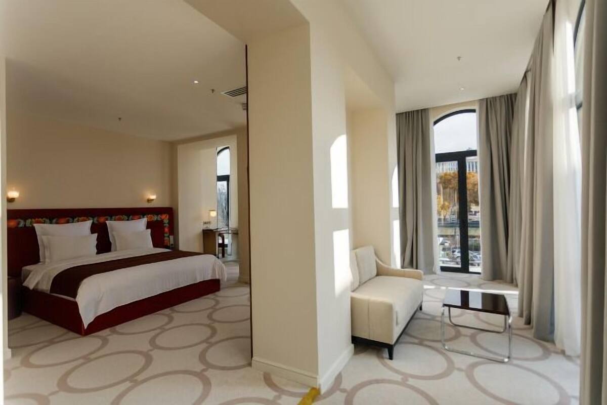 A hotel room with a bed, a sofa, a small table, and a view of the outside.
