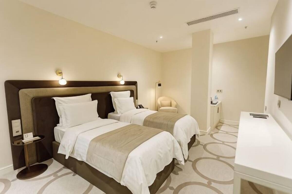 A hotel room with two beds, a desk, a chair, a TV, and a bathroom.
