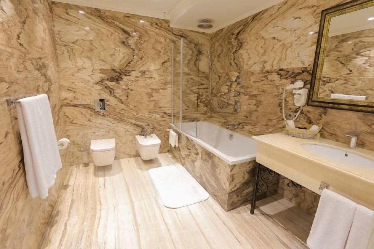 A bathroom with marble walls, a bathtub, a sink, and a shower.