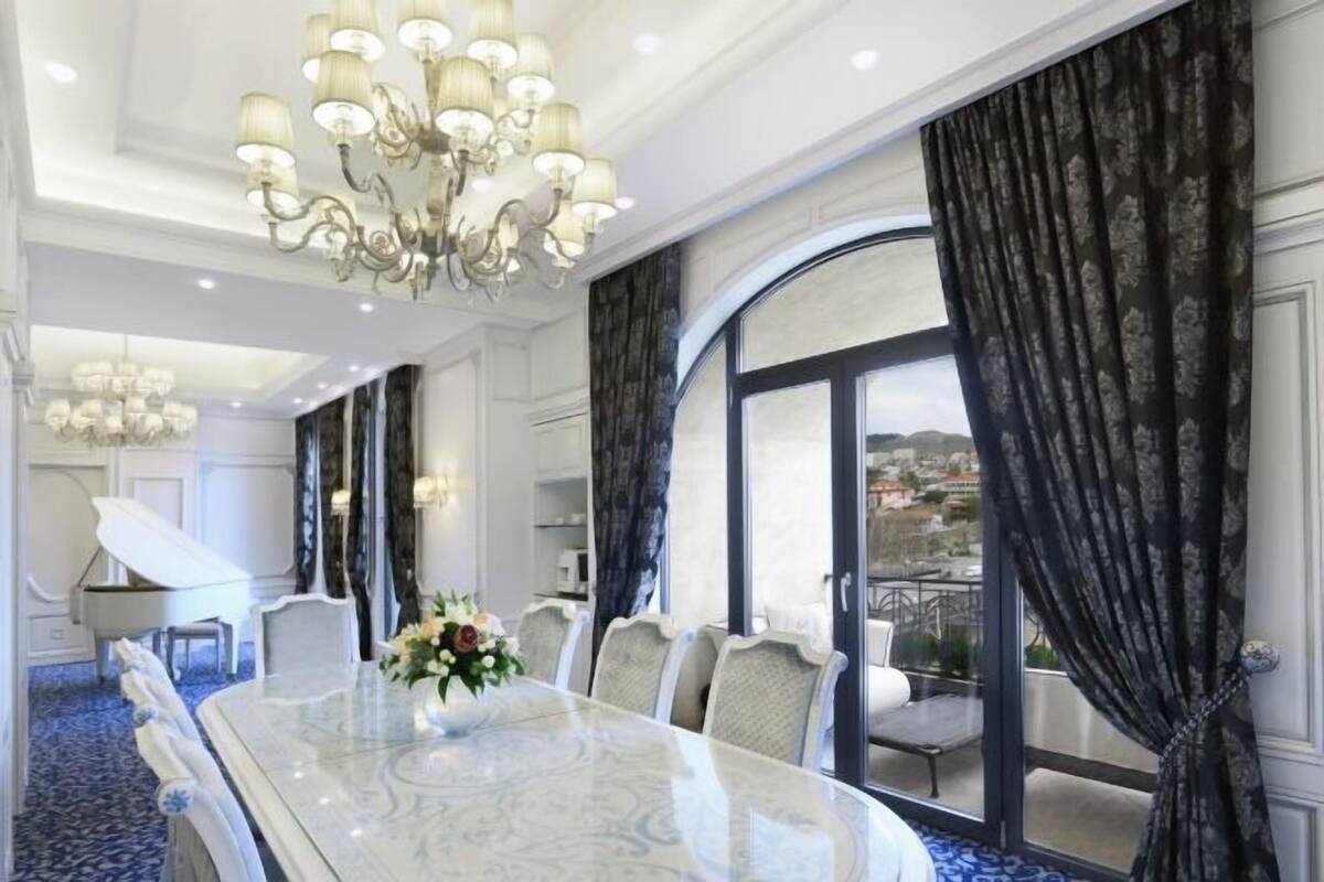 A dining room with a large table, chairs, a chandelier, and a view through a large window.